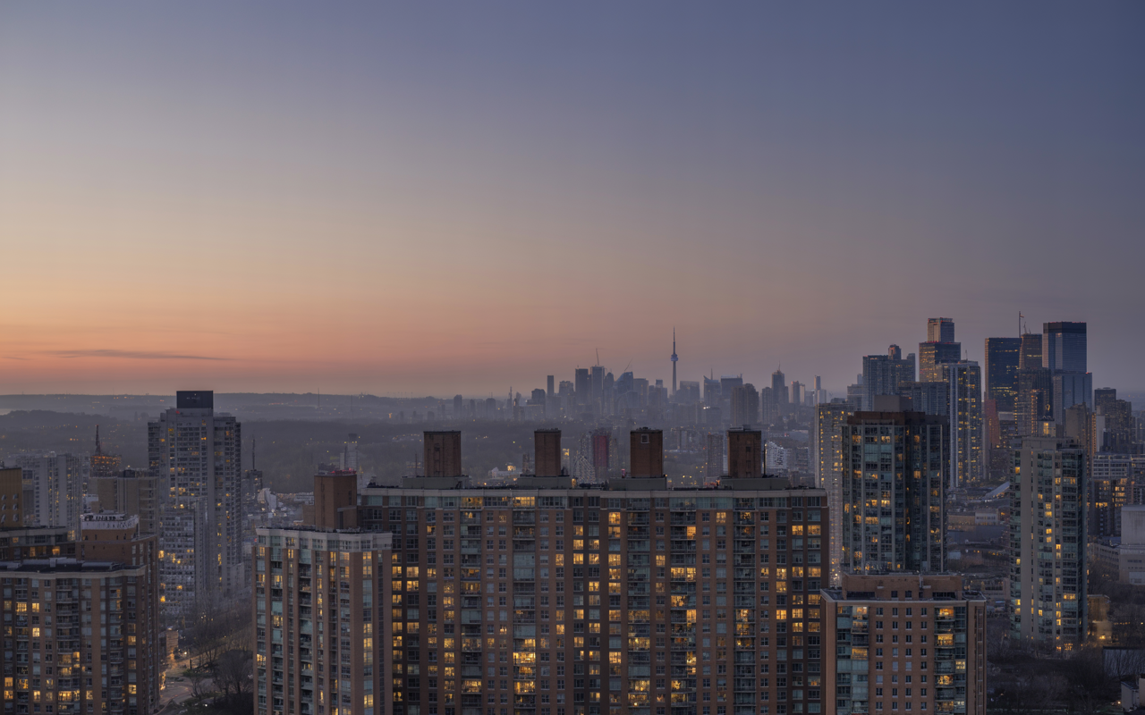 Toronto rental market at dusk showing mid-rise and high-rise apartment buildings with unevenly lit units, reflecting softening demand and rising housing supply.